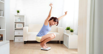 Happy woman standing on a BMI scale in her living room, tracking fitness progress