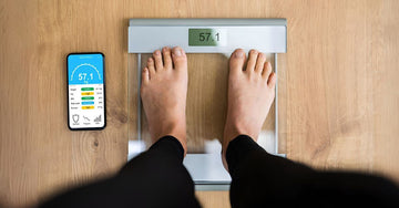 Man standing on a smart scale with a smartphone displaying the connected scale app interface